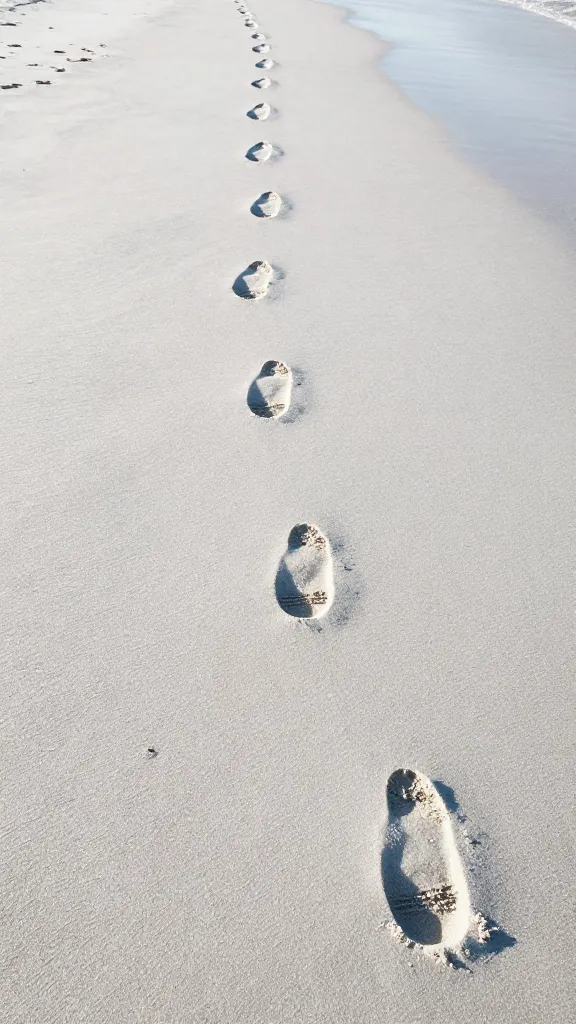 Sunrise stroll on white sand shoreline, footprints in wet sand