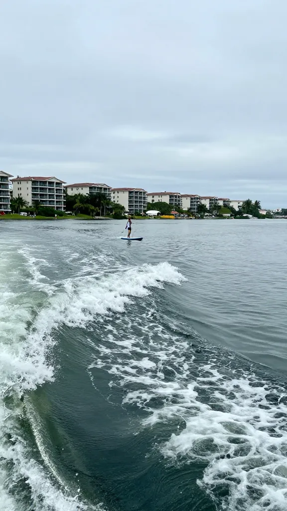 Paddleboard wake near condo-lined shoreline, calm Gulf water